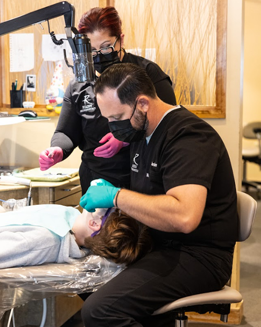 Orthodontist in black gloves examining patient's teeth in modern dental clinic treatment room.