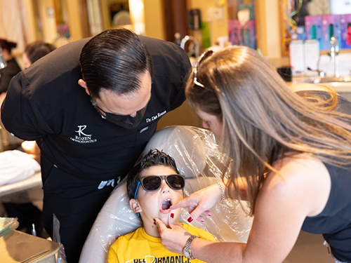Orthodontist fitting sunglasses on young patient while staff member assists in modern dental office.