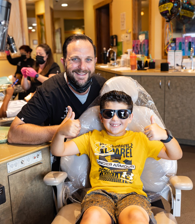 Adult and child smile together in orthodontic office reception area.