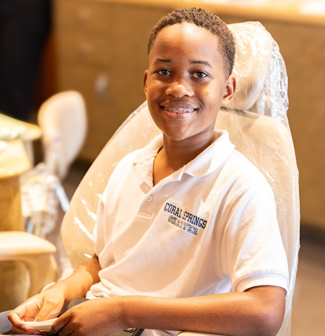 Young person smiling at orthodontic office desk wearing Rozen Orthodontics branded shirt.