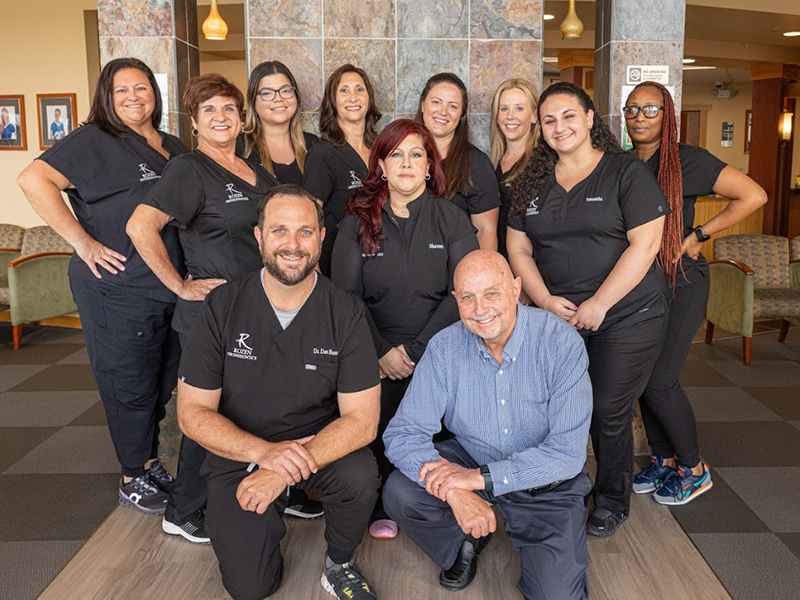 Rozen Orthodontics team posing together in professional black uniforms in indoor office setting.